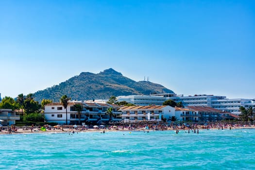 Mallorca, Spain, June 2015 People, tourists enjoying sun holidays on Alcudia beach, view from turquoise sea on sandy beach and mountain in background