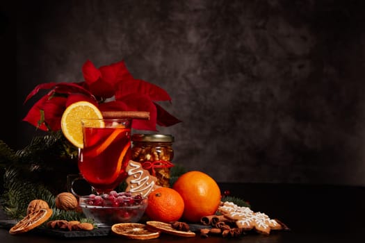 Still life with glasses of mulled wine or fruit tea, Red Poinsettia flowers, fir branch and spices on a dark background with copy space. New year and Christmas table setting. Greeting card.