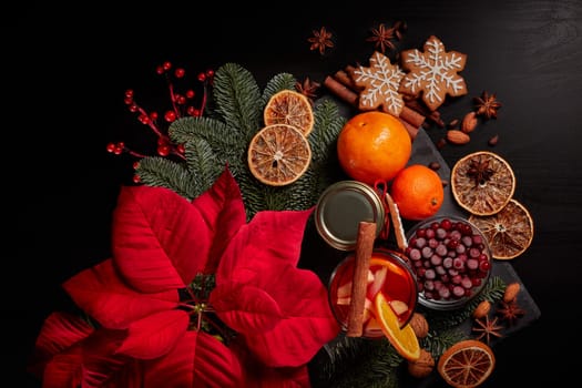 Still life with glasses of mulled wine or fruit tea, Red Poinsettia flowers, fir branch and spices on a dark background. Top view. New year and Christmas table setting. Greeting card.