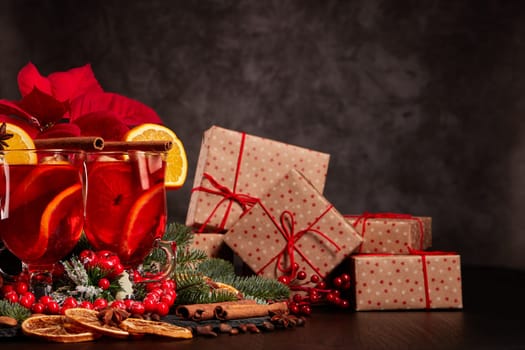 Still life with glasses of mulled wine or fruit tea, Red Poinsettia flowers, fir branch and gift boxes on a dark background with copy space. New year and Christmas table setting. Greeting card.