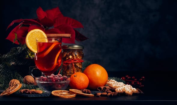 Still life with glasses of mulled wine or fruit tea, Red Poinsettia flowers, fir branch and spices on a dark background with copy space. New year and Christmas table setting. Greeting card.