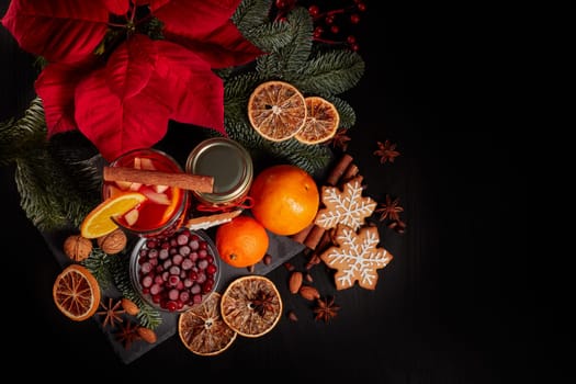 Still life with glasses of mulled wine or fruit tea, Red Poinsettia flowers, fir branch and spices on a dark background. Top view. New year and Christmas table setting. Greeting card.
