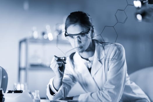 Portrait of a confident female health care expert in life science laboratory writing structural chemical formula on a glass board. Healthcare and modern life science concept. Blue toned image.