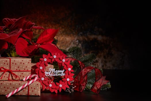 Christmas decoration with Red Poinsettia flowers (Euphorbia Pulcherrima), fir branch and gift boxes on a dark background. Christmas background with copy space. Greeting card.
