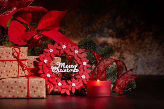 Christmas decoration with Red Poinsettia flowers (Euphorbia Pulcherrima), fir branch, burning candle and gift boxes on a dark background. Christmas background with copy space. Greeting card.