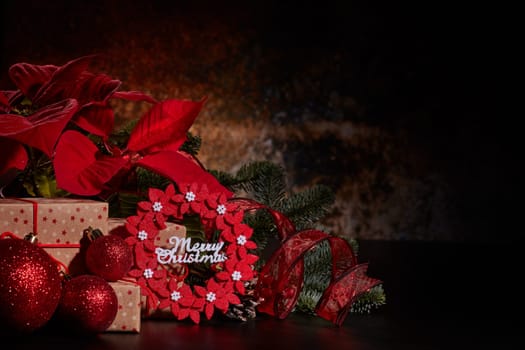 Christmas decoration with Red Poinsettia flowers (Euphorbia Pulcherrima), fir branch and gift boxes on a dark background. Christmas background with copy space. Greeting card.