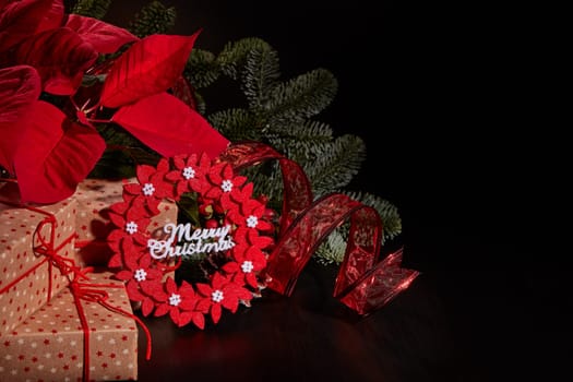 Christmas decoration with Red Poinsettia flowers (Euphorbia Pulcherrima), fir branch and gift boxes on a black background. Christmas background with copy space. Greeting card.