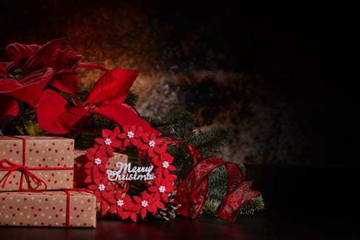 Christmas decoration with Red Poinsettia flowers (Euphorbia Pulcherrima), fir branch and gift boxes on a dark background. Christmas background with copy space. Greeting card.