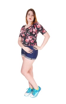 A lovely young woman standing in the studio in jeans shorts and a .colorful blouse and sneakers, isolated for white background.