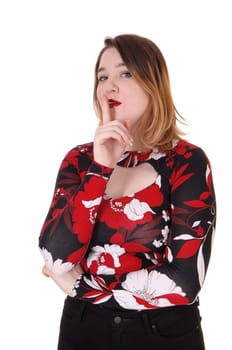 A beautiful young woman in a colorful blouse and blond hair standing.with one finger over her mouths, be quiet, isolated for white .background.