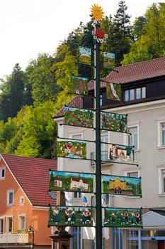 Large tree shaped signpost with pictures connected to sides and yellow smiling sun on top. Forest and houses in background.