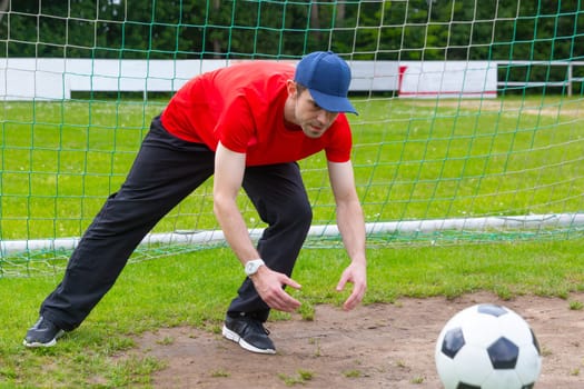 Young man with cap as goalkeeper catching a soccer ball on a soccer field