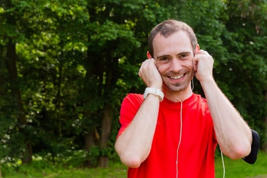 Friendly young sportsman with earphones outdoor in a park