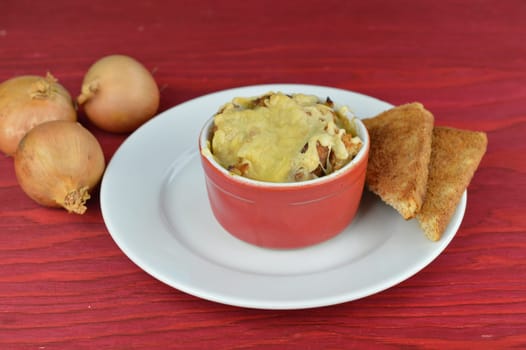 onion soup au gratin with bread and cheese on red wooden table with onions as traditional autumnal food