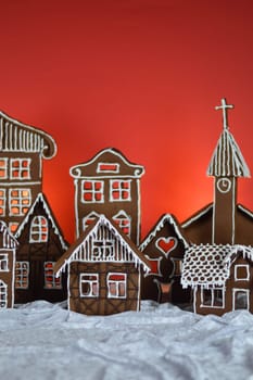 home made sweet delicious baked gingerbread village with church in front of red background on white snowlike velvet as traditional christmas decoration for the family
