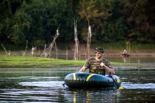 The smiling man is rowing and enjoying in inflatable boat on lake.