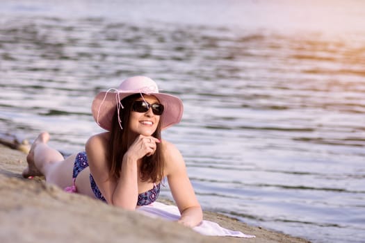 The smiling sunbathing woman is enjoying in the summer lying down on sand on the beach.