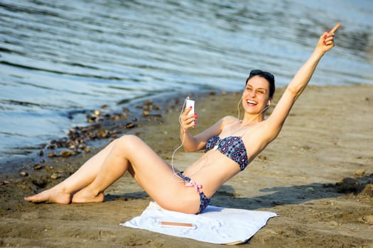 The attractive cheerful woman in bikini is having fun and using phone on the beach, summer lifestyle.