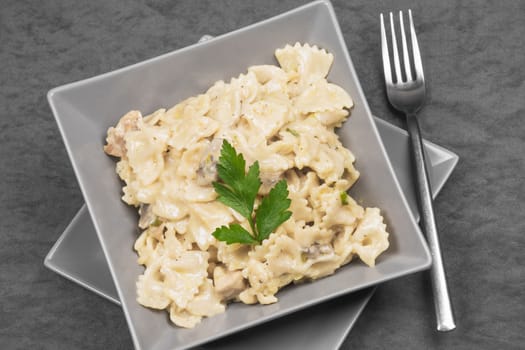 Pasta in cheese sauce with parsley Italian food in gray plate on gray background.