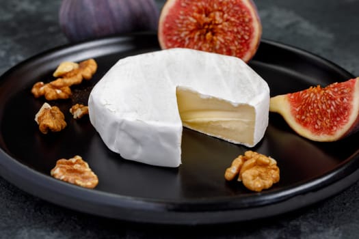 Camembert cheese on a ceramic dish with peeled walnuts and figs