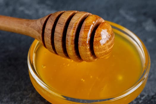 Honey in a glass bowl and a wooden stick for honey on a dark background