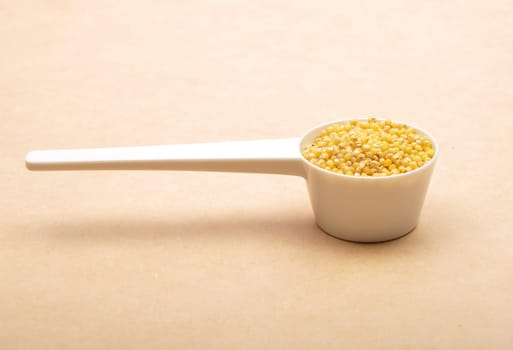 Raw millet in  measuring spoon on brown background