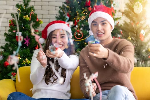 Young asian adult teenager couple celebrateing christmas holiday together with Firecrackers in living room with christmas tree decoration.