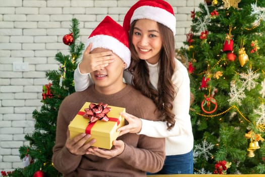 beautiful asian girl give surprise christmas gift to her boyfriend in Christmas holiday season greeting.