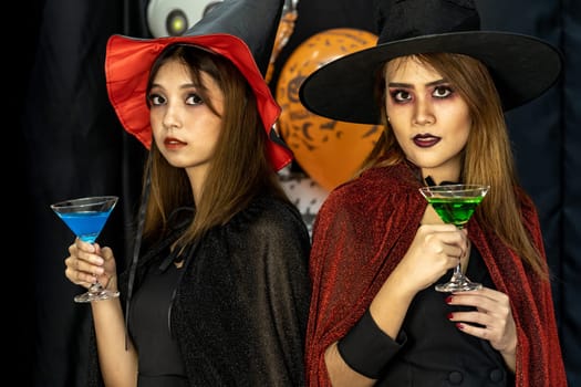 Two young adult and teenager girls celebrating a Halloween party carnival Festival in Halloween costumes drinking alcohol cocktail