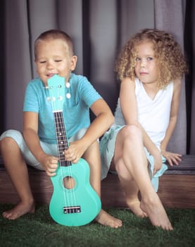 Portrait of a cute kids sitting ouddoor with ukulele