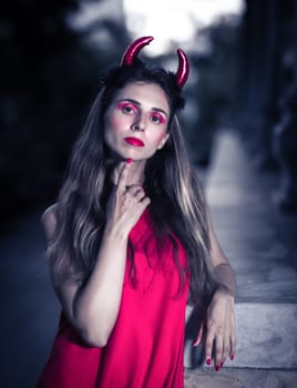 Fashion portrait of a beautiful woman in red dress and horns. Halloween