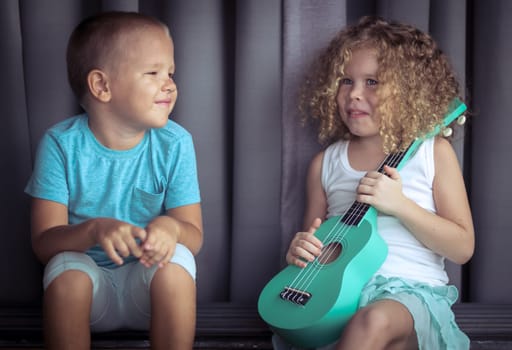 Portrait of a cute kids sitting ouddoor with ukulele