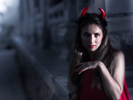 Fashion portrait of a beautiful woman in red dress and horns. Halloween