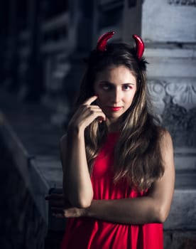 Fashion portrait of a beautiful woman in red dress and horns. Halloween