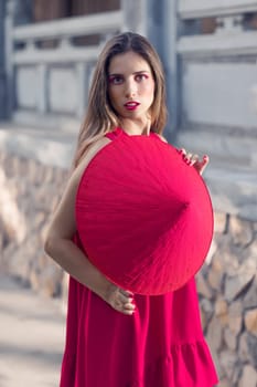 Fashion portrait of a beautiful woman in red conical hat outdoor