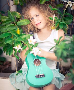 Portrait of a cute girl sitting ouddoor with ukulele