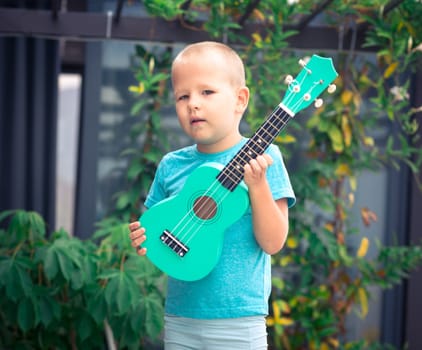 Portrait of a cute boy sitting ouddoor with ukulele