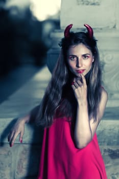 Fashion portrait of a beautiful woman in red dress and horns. Halloween