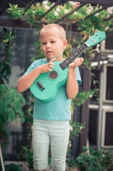 Portrait of a cute boy sitting ouddoor with ukulele