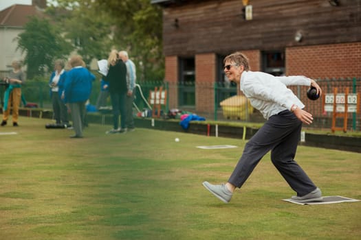 A side view shot of an excited senior woman taking her shot in a game of lawn bowling.
