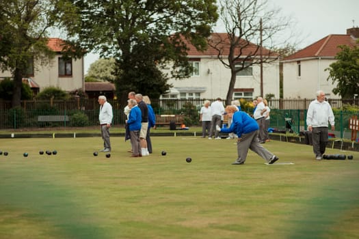 A side view shot of a senior woman taking her shot in a game of lawn bowling, surrounded by other seniors in the community.