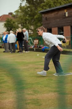 A side view shot of a senior woman taking her shot in a game of lawn bowling.
