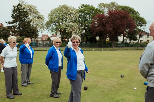 A front view shot of a group of senior women giving their thumbs up at a bowling green.