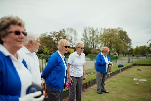 A small group of senior friends watching the lawn bowling game, standing on grass.