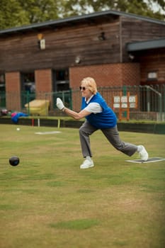 A side view shot of a senior woman taking her shot in a game of lawn bowling.