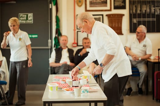 A side view shot of a senior man adding jam to his scones.