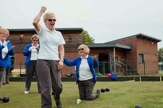 A small group of senior women celebrating during lawn bowling, with one woman punching the air.