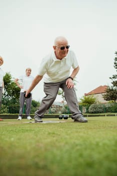 A front view shot of a senior man taking his shot in a game of lawn bowling.
