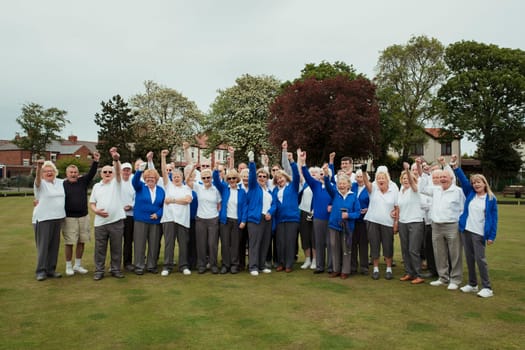 A wide view shot of a community of seniors punching the air, celebrating after their lawn bowling game.