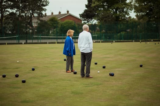 Two senior adults standing together in the middle of a bowling green, surrounded by bocce balls.